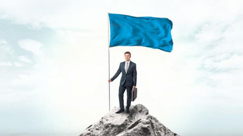 Businessman on the top of a the mountain holding flag