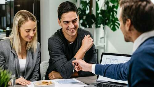 Young happy couple going through housing plans with real estate agent.