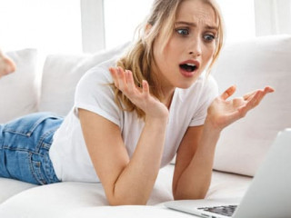 Portrait of outraged girl 20s using laptop while lying on couch