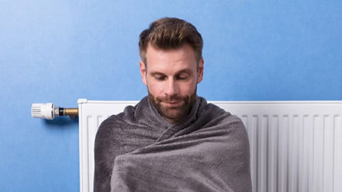 Man Sitting In Front Of Heater At Home