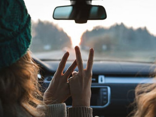 two friends or sisters travelling by car, showing peace sign