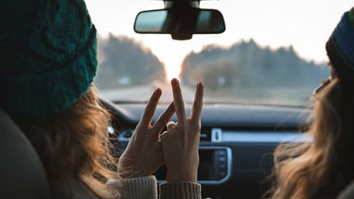 two friends or sisters travelling by car, showing peace sign