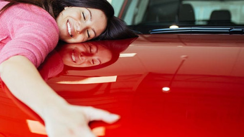 Happy beautiful young woman buying a new car at the car showroom