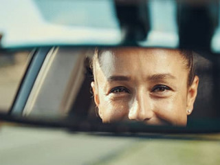 Happy woman looking at her face in rear-view mirror