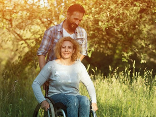 Smiling woman in wheelchair with husband in the park on sunny day
