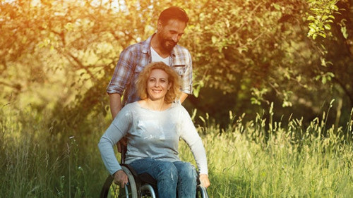 Smiling woman in wheelchair with husband in the park on sunny day