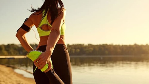 Young woman runner doing warm-up stretching her legs in a park.