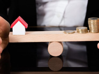 Model House And Money Coins Balancing On A Seesaw
