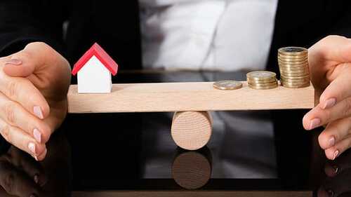 Model House And Money Coins Balancing On A Seesaw
