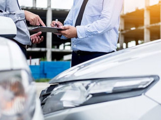Insurance agent writing on clipboard while examining car after a