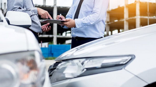 Insurance agent writing on clipboard while examining car after a