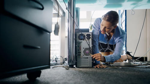 Young secretary connecting cables to pc in office