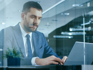 Confident Handsome Businessman Works on a Laptop at His Desk. St