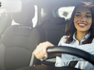 Beautiful young happy smiling woman driving her new car at sunse
