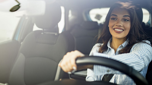 Beautiful young happy smiling woman driving her new car at sunse