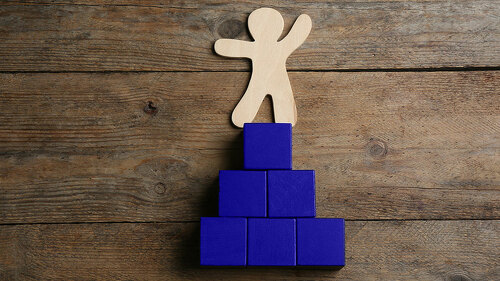 Human figure and pyramid on wooden background, flat lay. Career