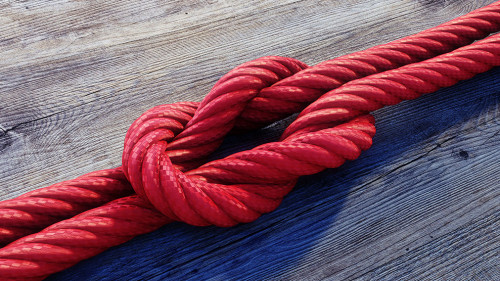 Kreuzknoten mit rotem Seil auf Holz