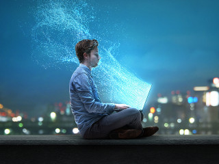 Mann sitzt am Notebook vor nächtlicher Stadt