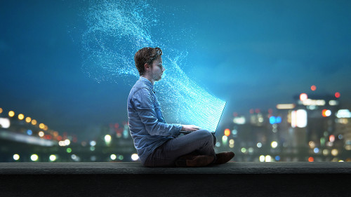 Mann sitzt am Notebook vor nächtlicher Stadt