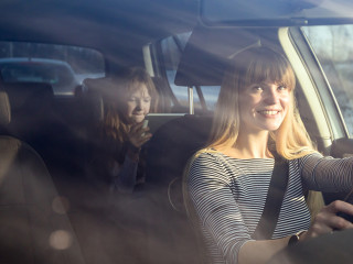 Mom driving car while her daughter sitting on back seat and usin