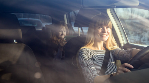 Mom driving car while her daughter sitting on back seat and usin