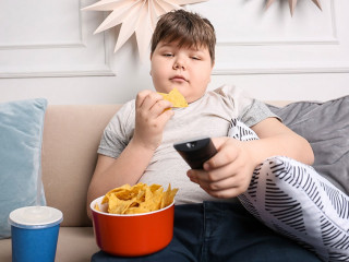 Overweight boy watching TV with snacks indoors