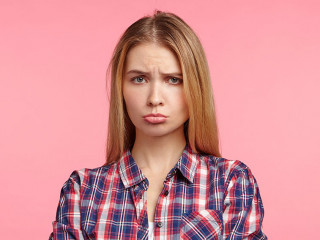 Portrait of offened unhappy beautiful woman keeps hands crossed, curves lips, displeased with everything, being abused by bad words and remarks from best friend, feels frustrated and very upset