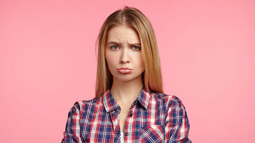 Portrait of offened unhappy beautiful woman keeps hands crossed, curves lips, displeased with everything, being abused by bad words and remarks from best friend, feels frustrated and very upset