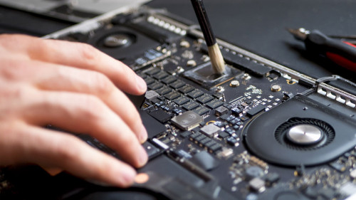 hand with brush clearing the disassembled laptop from dust and dirty close up in workshop