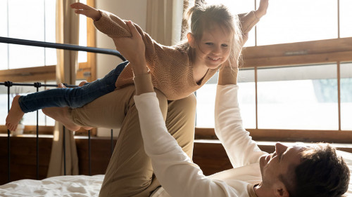 Loving dad playing with excited little daughter in home bedroom