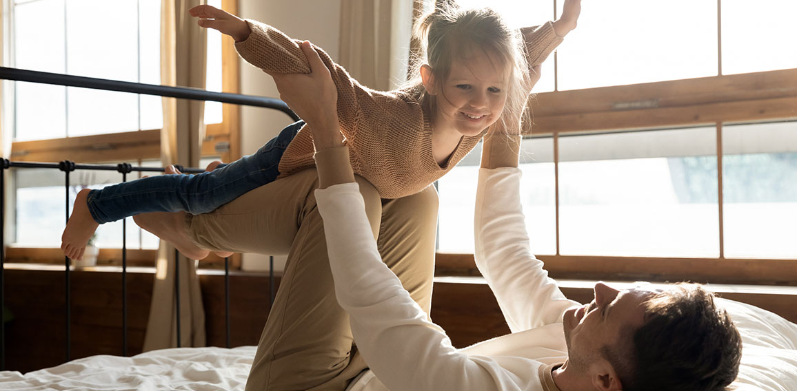 Loving dad playing with excited little daughter in home bedroom