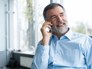 Executive senior businessman using his mobile phone and talking wih somebody while working laptop in the office.