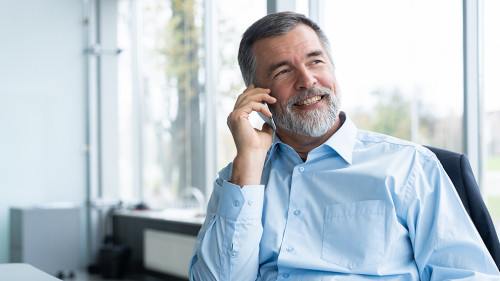 Executive senior businessman using his mobile phone and talking wih somebody while working laptop in the office.
