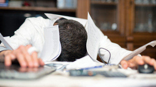 Desperate man submerged from work in his office. Papers and lapt