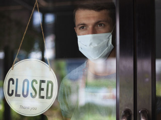 Chef in safety mask hanging up sign closed on restaurant door.