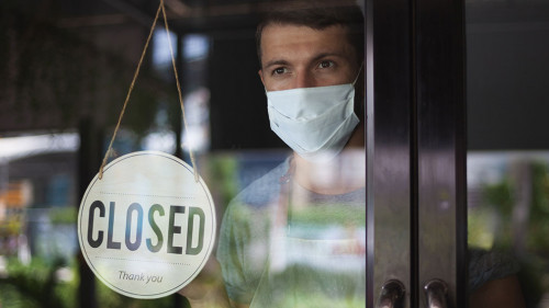 Chef in safety mask hanging up sign closed on restaurant door.