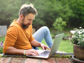 Mature man with laptop working outdoors in garden, home office concept.