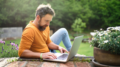 Mature man with laptop working outdoors in garden, home office concept.