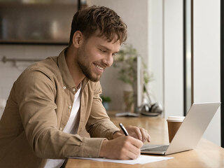 Close up smiling man using laptop, taking notes, studying online