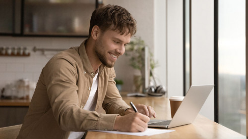 Close up smiling man using laptop, taking notes, studying online
