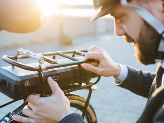 Hipster businessman commuter setting up electric bicycle in city.
