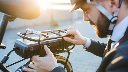 Hipster businessman commuter setting up electric bicycle in city.