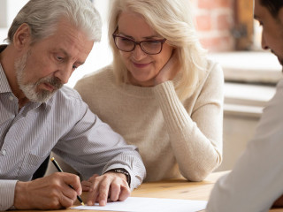 Happy mature couple close deal signing contract with realtor