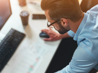 Work hard. Young bearded businessman in eyeglasses and formal wear using computer while standing in the modern office