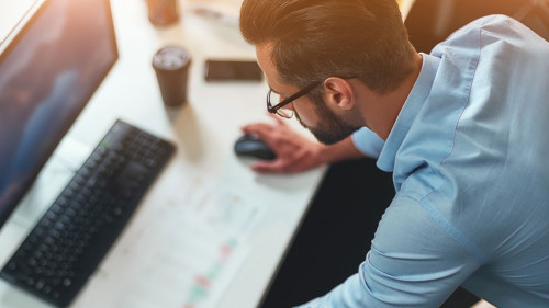 Work hard. Young bearded businessman in eyeglasses and formal wear using computer while standing in the modern office