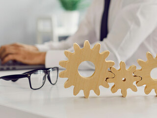 Three cogwheels joined together placed on desk against blurred background of busy office room