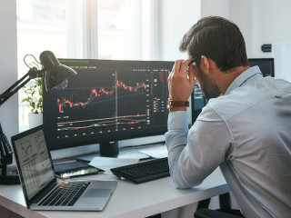 Working process. Smart male trader looking at charts on multiple computer screens and analyzing data while sitting in his modern office