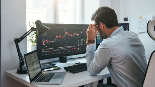 Working process. Smart male trader looking at charts on multiple computer screens and analyzing data while sitting in his modern office