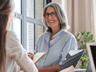Senior business woman working on laptop with assistant writing notes.