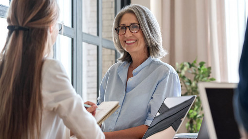 Senior business woman working on laptop with assistant writing notes.